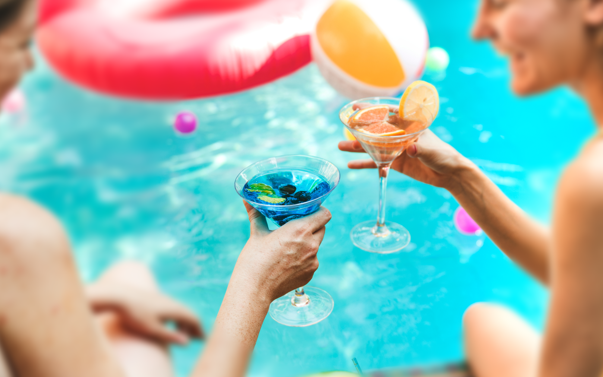 Two women drink together by a pool