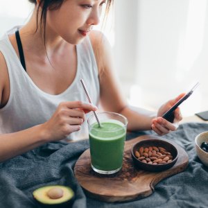 Woman with green smoothie reading on her phone